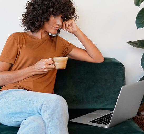 Mujer tomando café con leche en taa Nespresso mientras revisar ordenador portátil