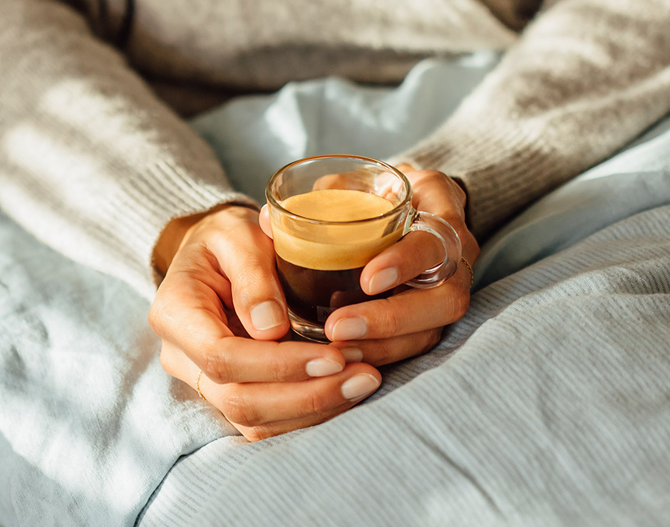 Dos manos sujetando taza de café de Nespresso en regazo encima de una manta