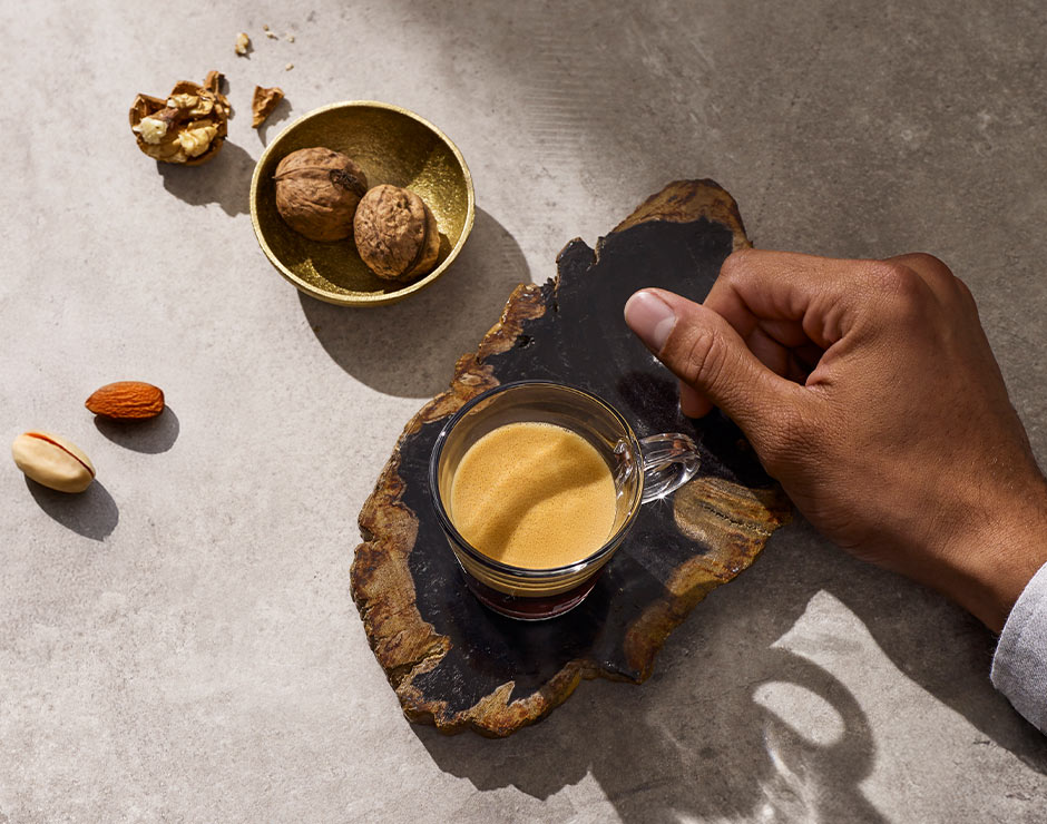 Mano cerca de una taza de café de Nespresso encima de un soporte de madera y frutos secos