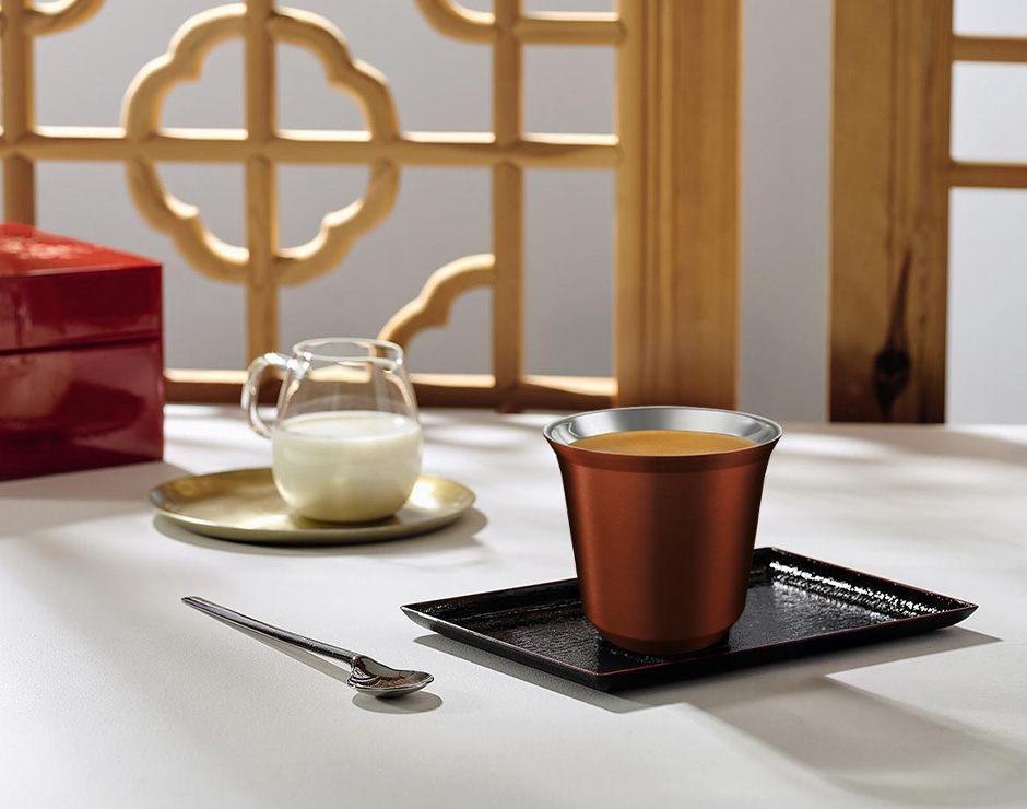 Café servido en vaso metálico junto a jarra con leche