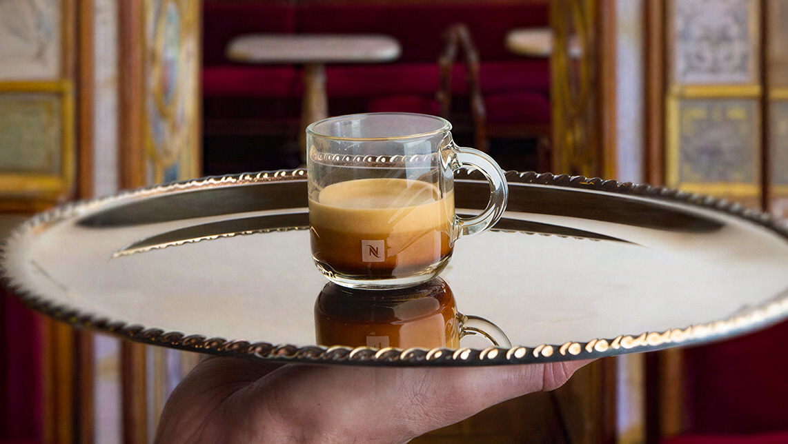 Bandeja plateada con café Nespresso servido en taza transparente