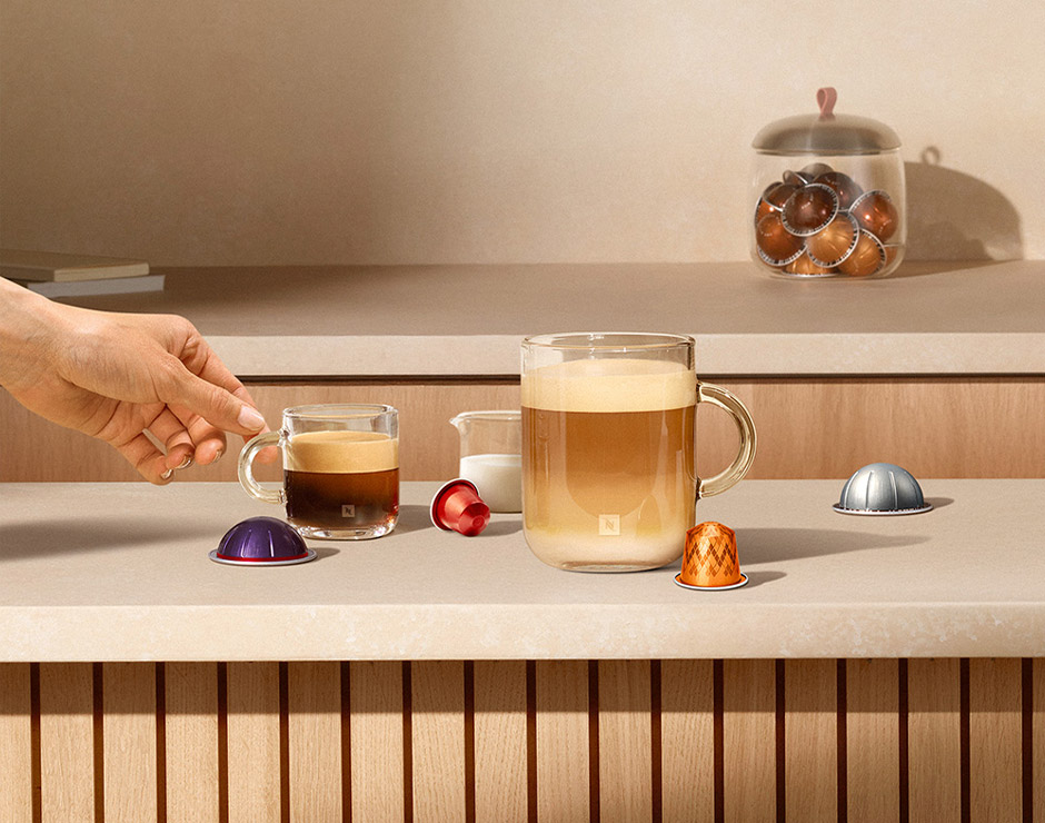 Café espumoso en vaso de cristal junto a cápsulas de café de varios colores