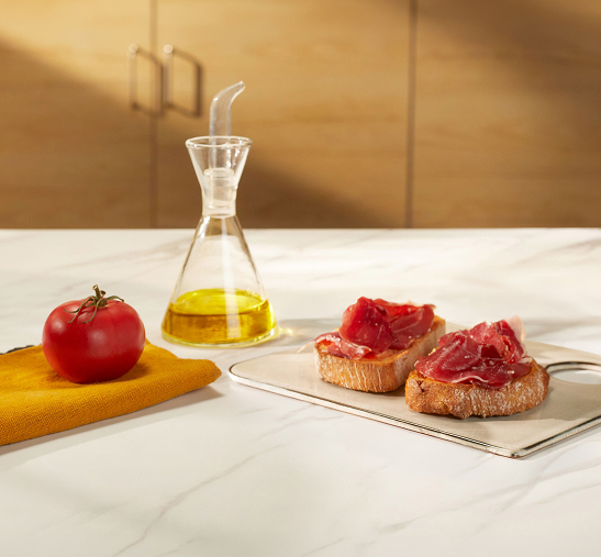 Pan con tomate y jamón junto a aceitera encima de mesa de mármol blanco