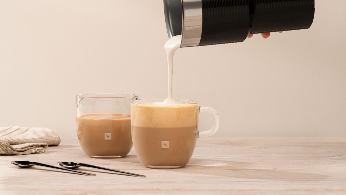 Espumador de leche encima de tazas transparentes