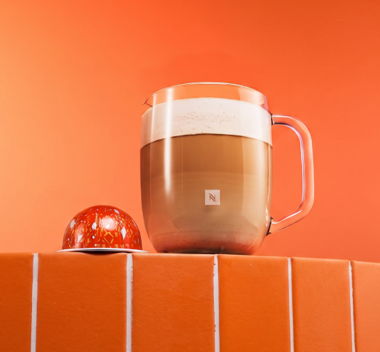 Taza de café con calabaza junto a la cápsula Nespresso Vertuo de color naranja