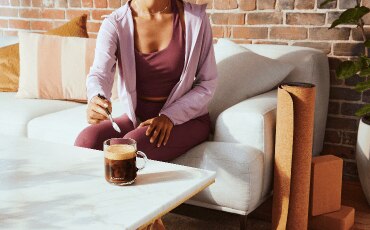Woman sitting on a couch stirring her Nespresso Vertuo coffee 