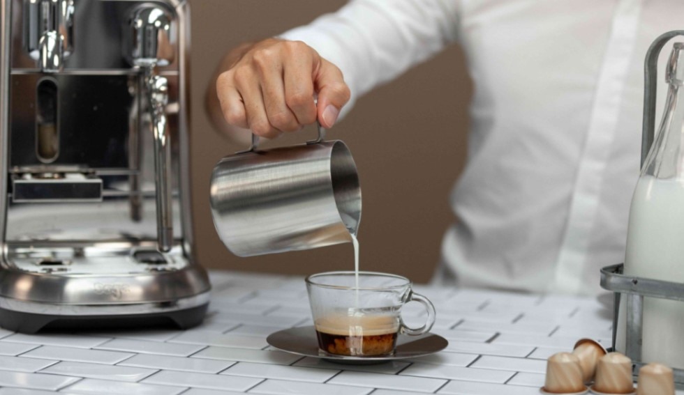 Person schenkt Milch mit einem Milchkännchen in einen Kaffee