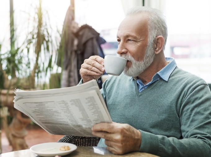 man drinking coffee while reading newspaper