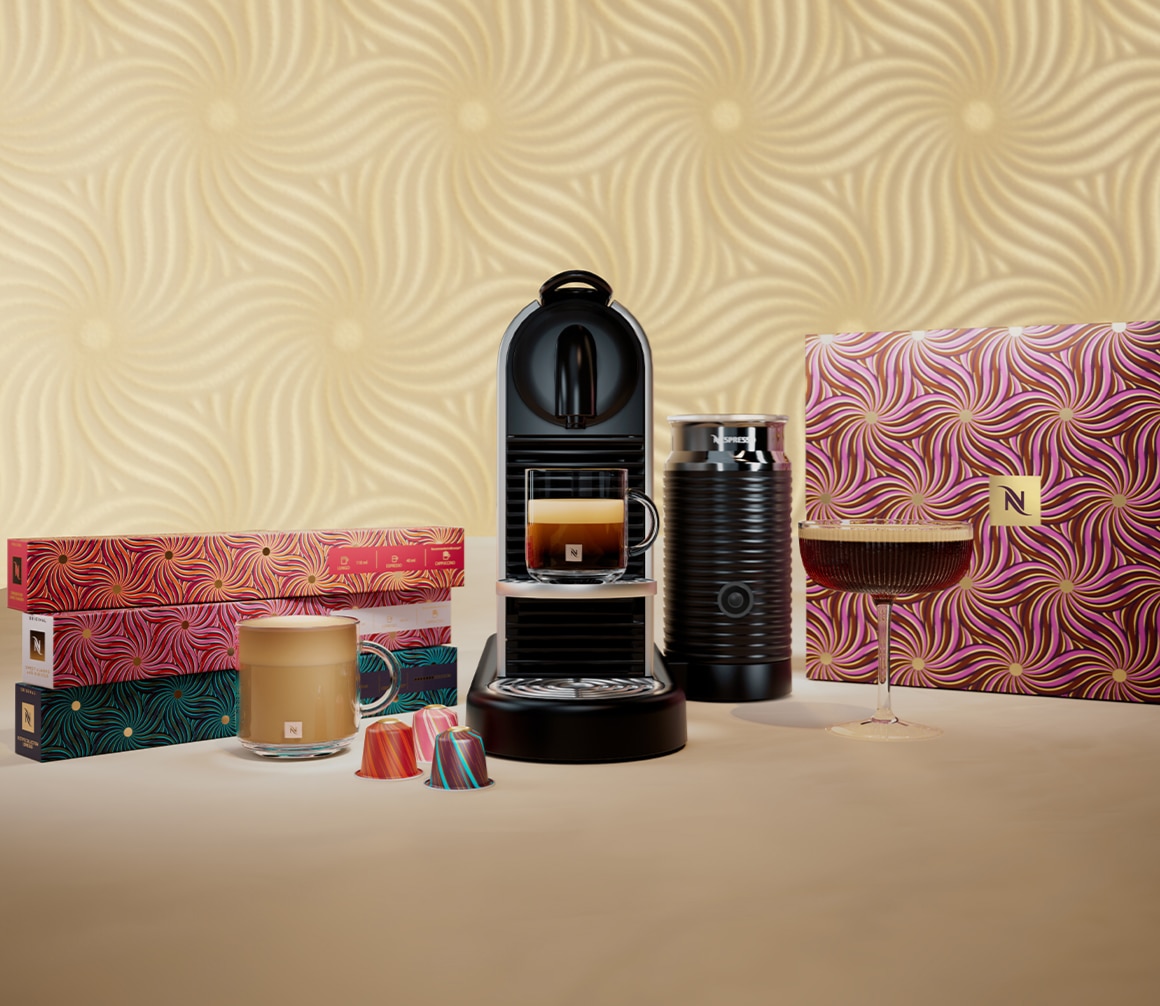 Nespresso Kaffeemaschine mit Milchaufschäumer, Festive-Kaffeekapseln in bunten Schachteln, Glas mit Kaffee und Cocktailglas auf beigem Hintergrund mit ornamentalem Muster. Rechts große Geschenkbox im gleichen Festive-Design.