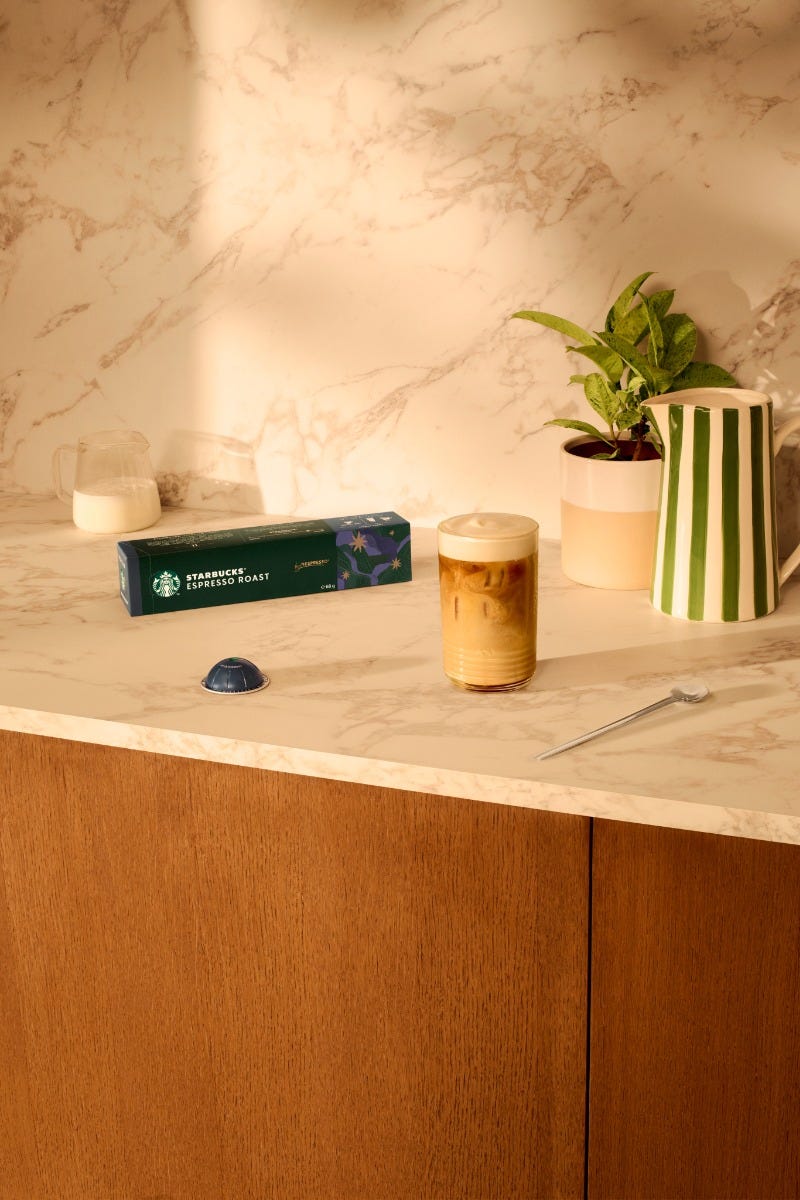 Starbucks&reg; Espresso Roast capsules beside an iced latte on a marble counter