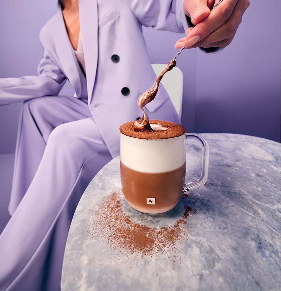 Person spooning a velvety cappuccino foam in a purple setup