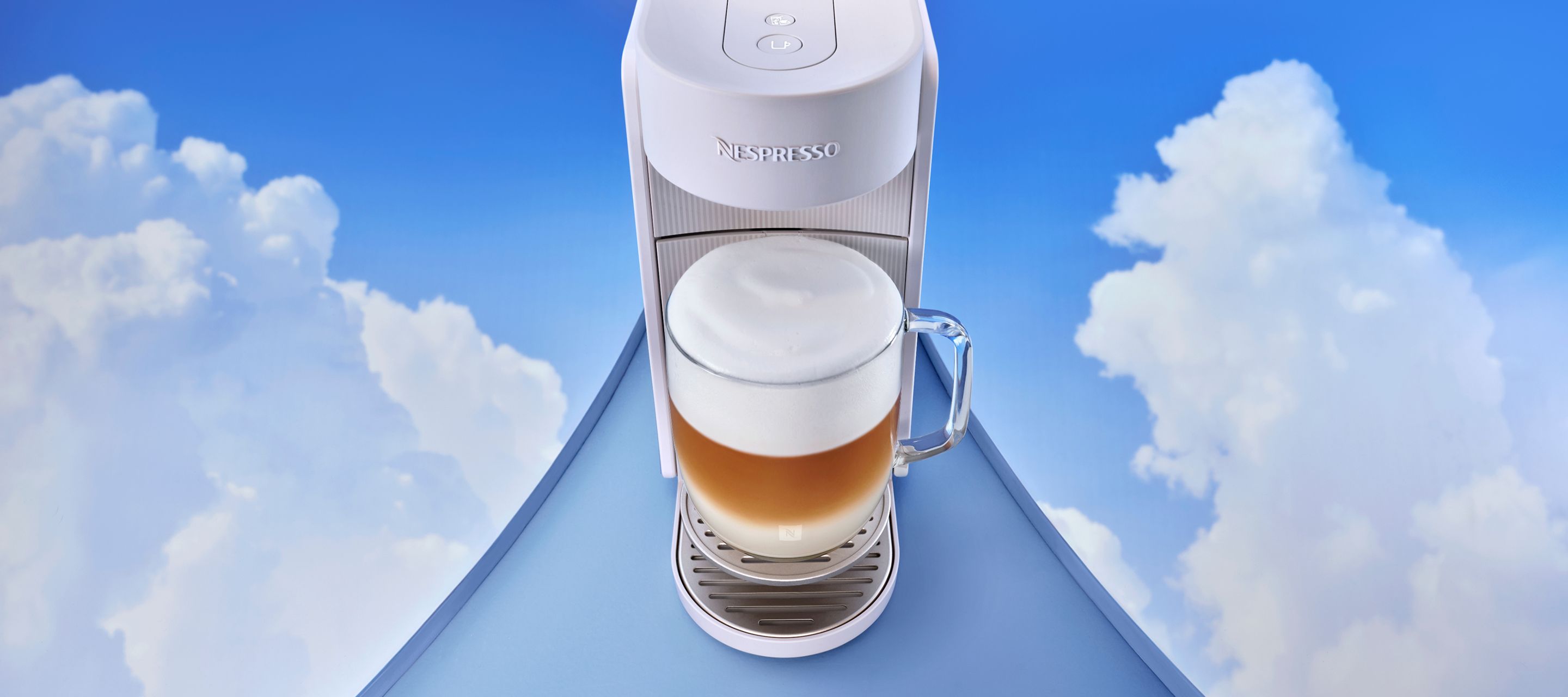 A coffee machine positioned on a cloud‑like blue platform with a freshly made coffee underneath.