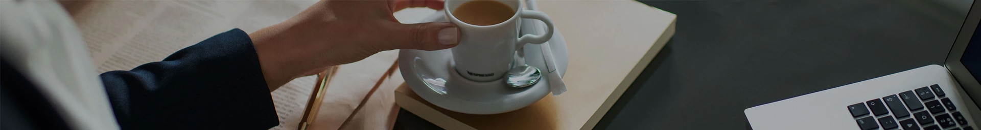 Person holding a Nespresso coffee cup with a computer next to it