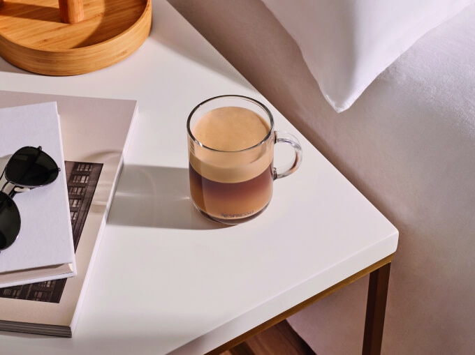 Délicieux cappuccino sur table blanche près de verres et livre.