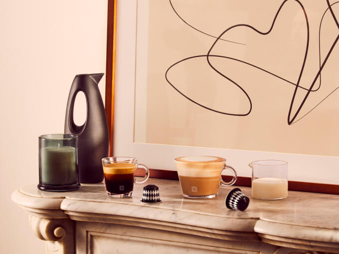 Trois tasses de café, deux capsules Nespresso, une bougie et une petite œuvre d'art sur console en marbre.