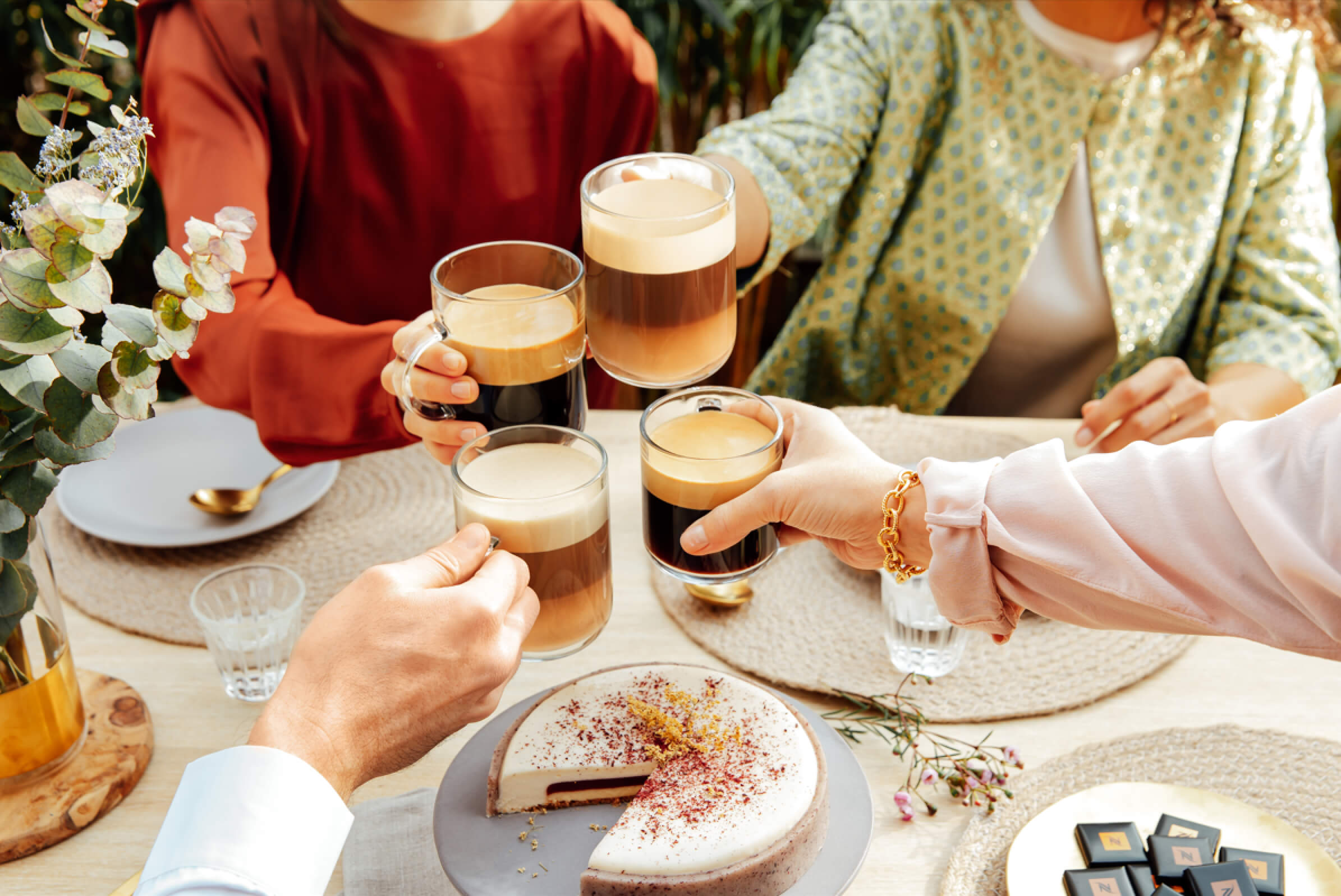 Four hands holding four different coffees and cheering. Discover the unique flavors of coffee with Nespresso Canada.