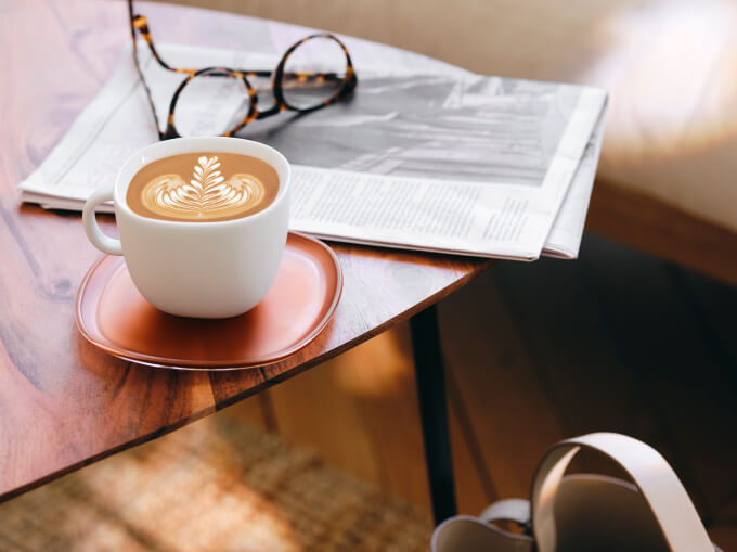Latte avec du latte art près d’une table basse, d’un journal et de lunettes.